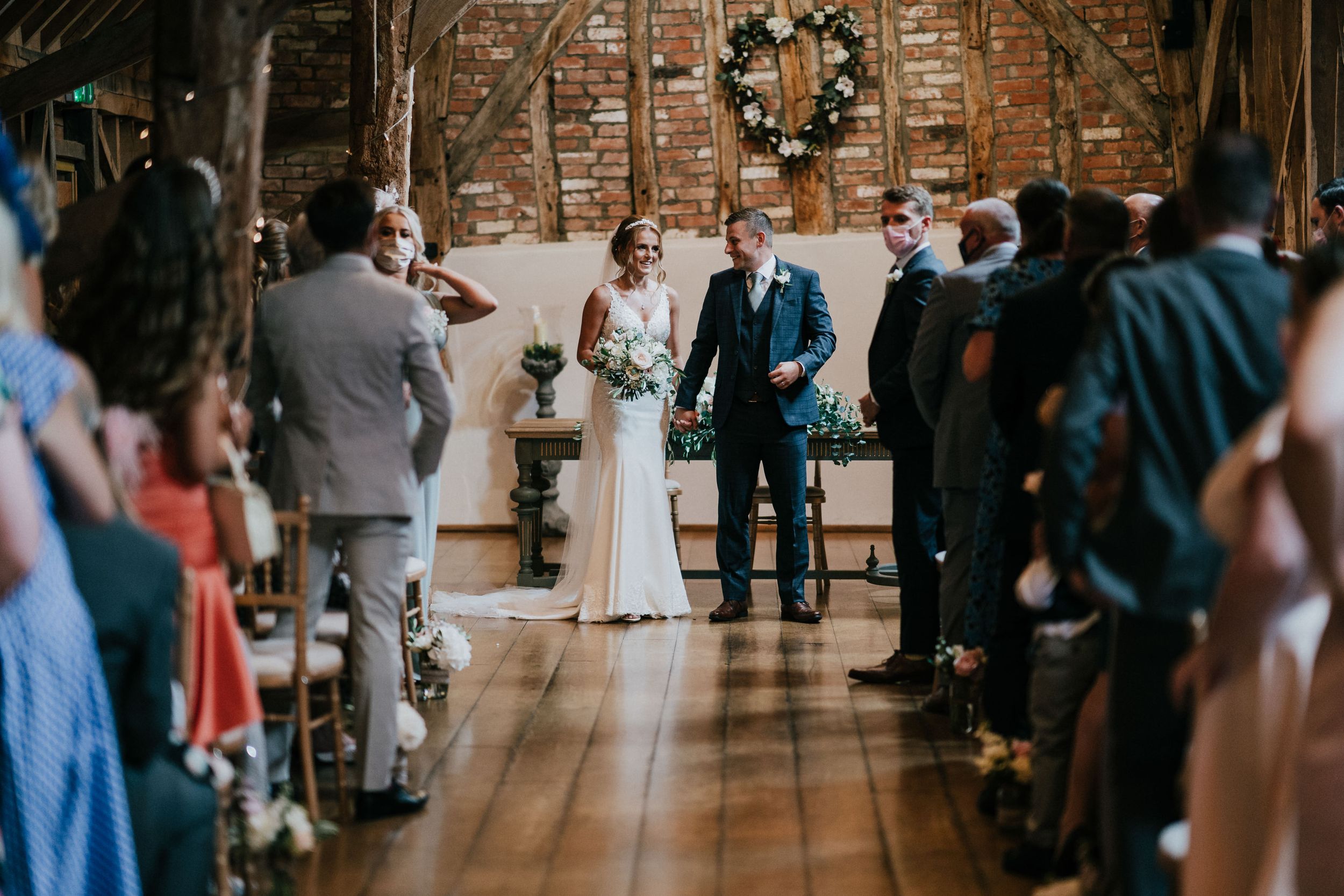 Intimate wedding ceremony at Rickety Barn in Bassmead taking place in a historic brick-walled venue with wooden floors and natural lighting.