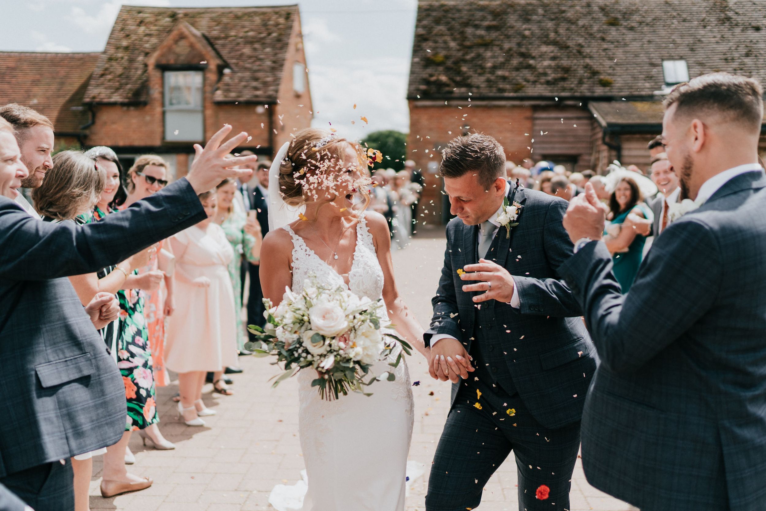 Wedding guests shower the newlyweds with confetti outside a Rickety Barn on a sunny day.