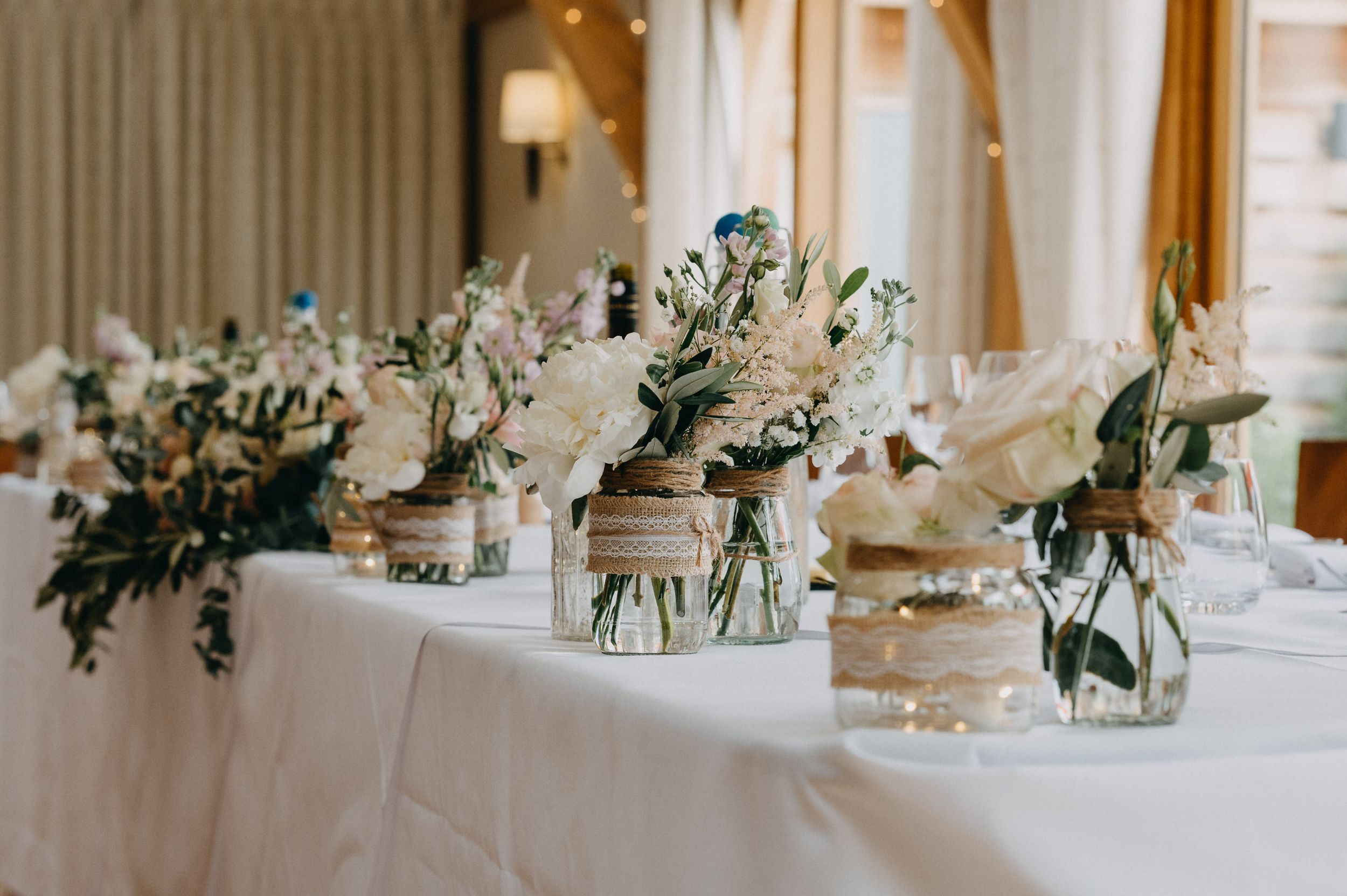 Elegant wedding table decorations at Bassmead Manor featuring white flowers and greenery in mason jars on crisp linens.