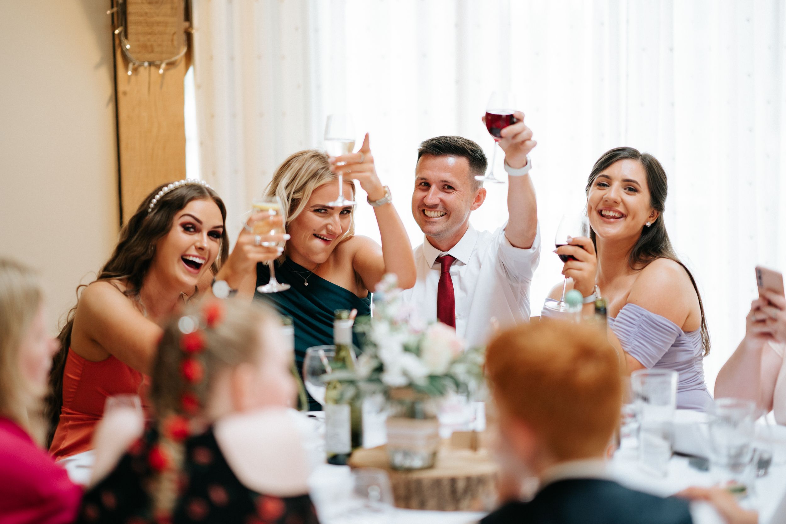 Wedding reception guests raise their glasses in celebration at a rustic indoor venue.