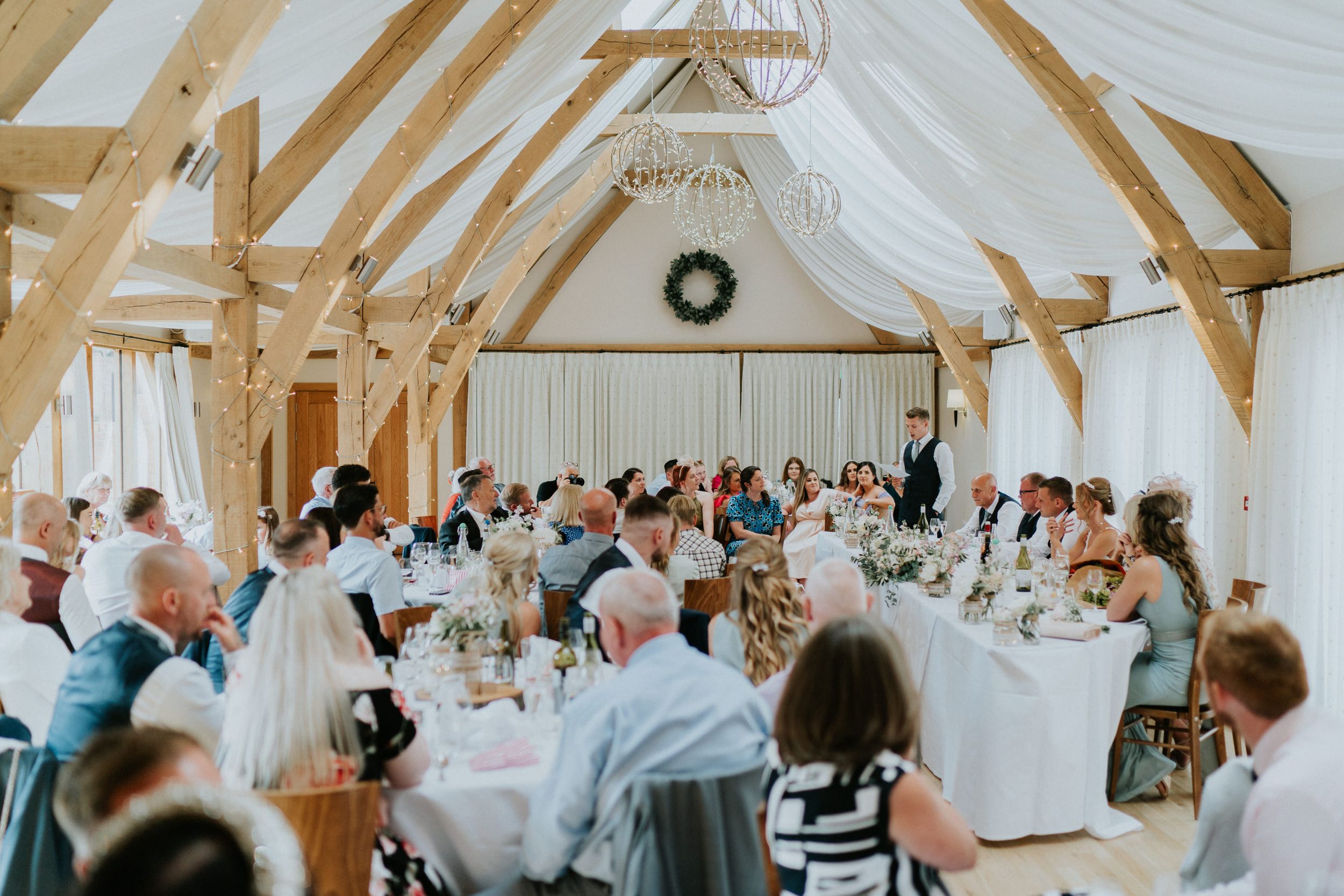 Wedding reception at Bassmead Manor Barns in a bright barn venue with exposed wooden beams and white drapery.