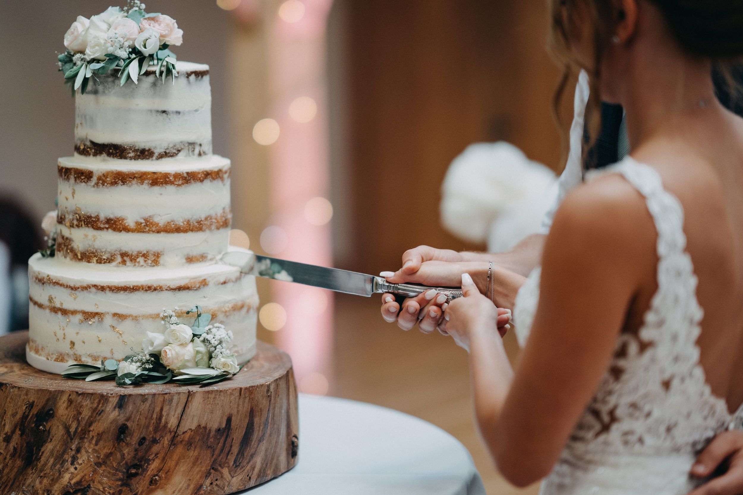 Semi-naked wedding cake with eucalyptus decoration being cut on rustic wood slice.