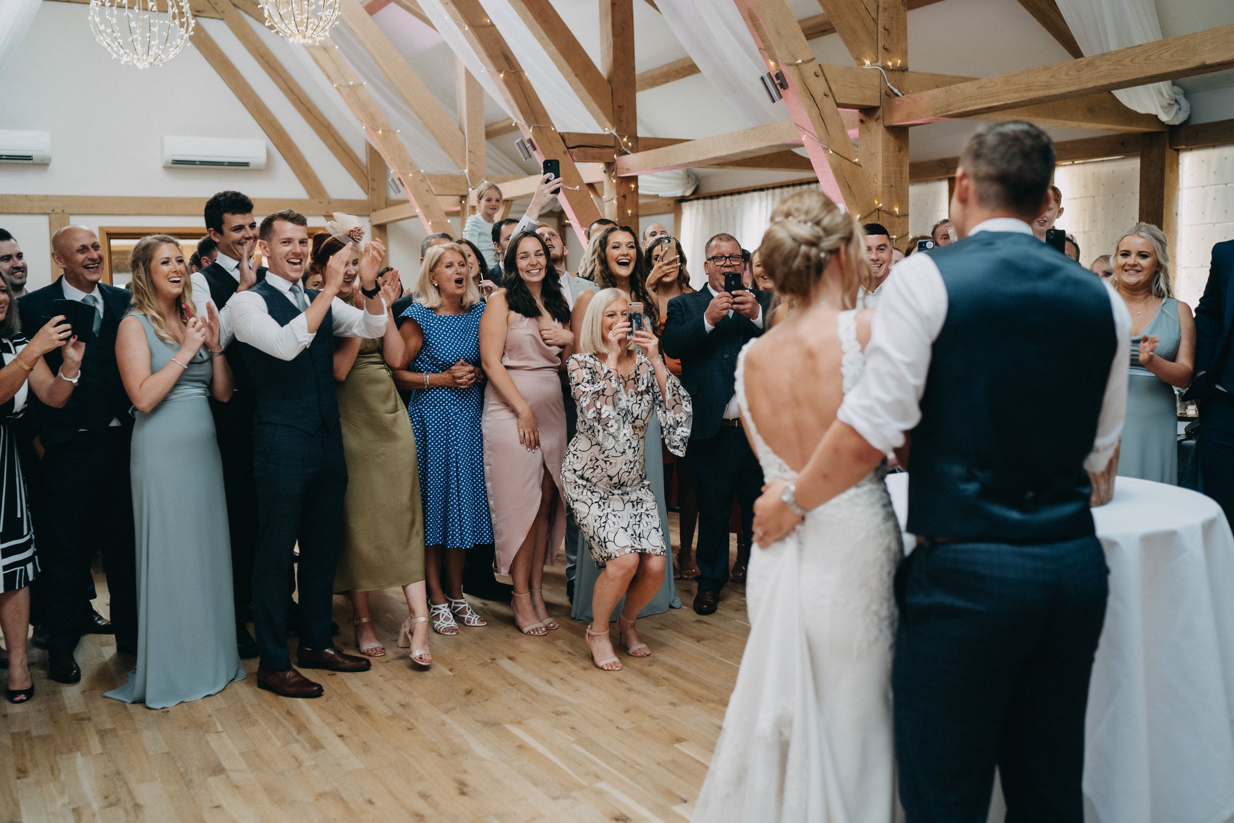 Wedding guests cheering during reception celebration in rustic wooden barn venue.