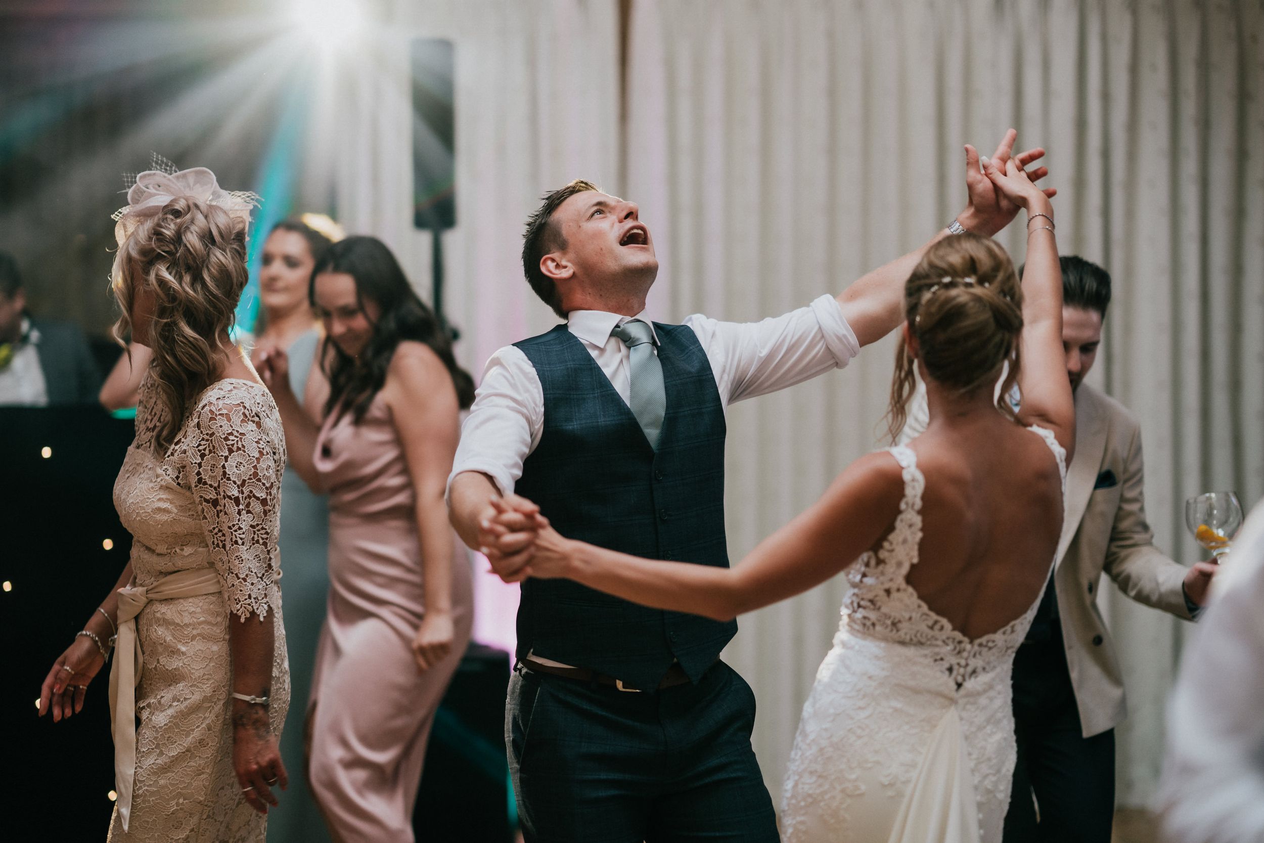 Guests dancing and celebrating at wedding reception in indoor venue.