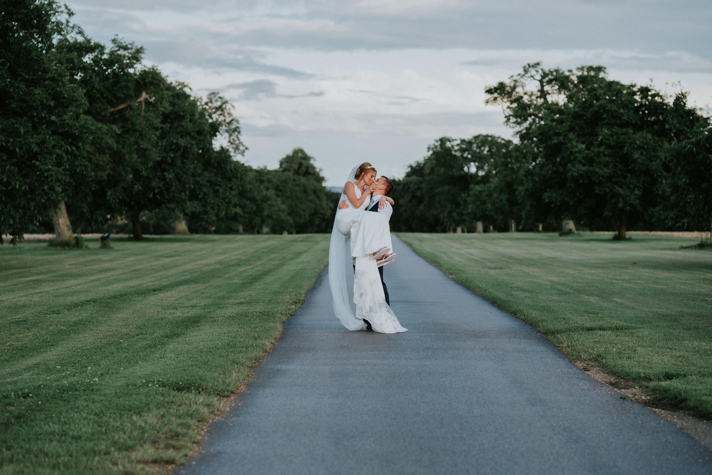 Couple embracing on tree-lined path during outdoor wedding portraits.