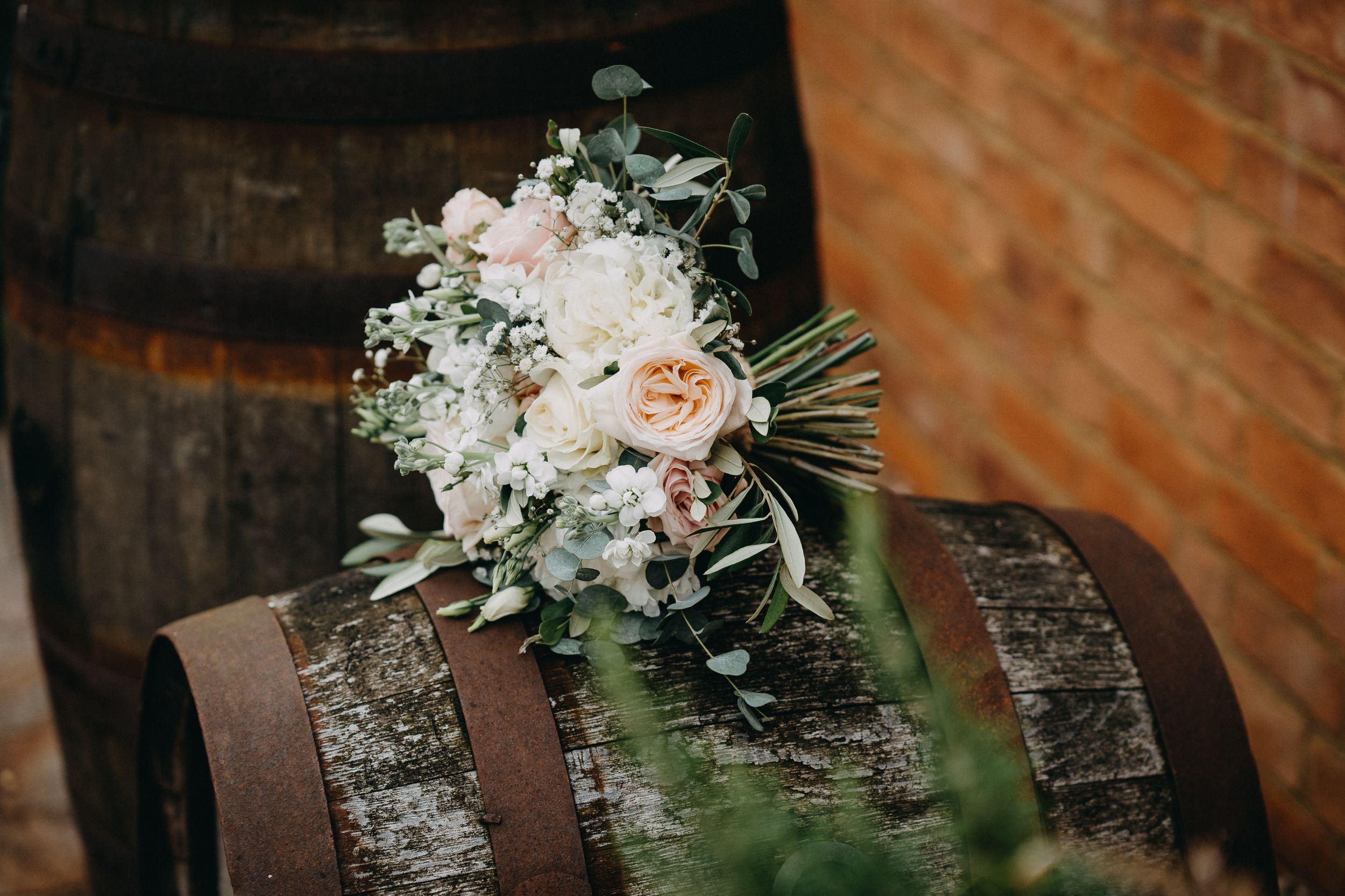 Romantic bridal bouquet with pink and white flowers resting on wooden barrel.