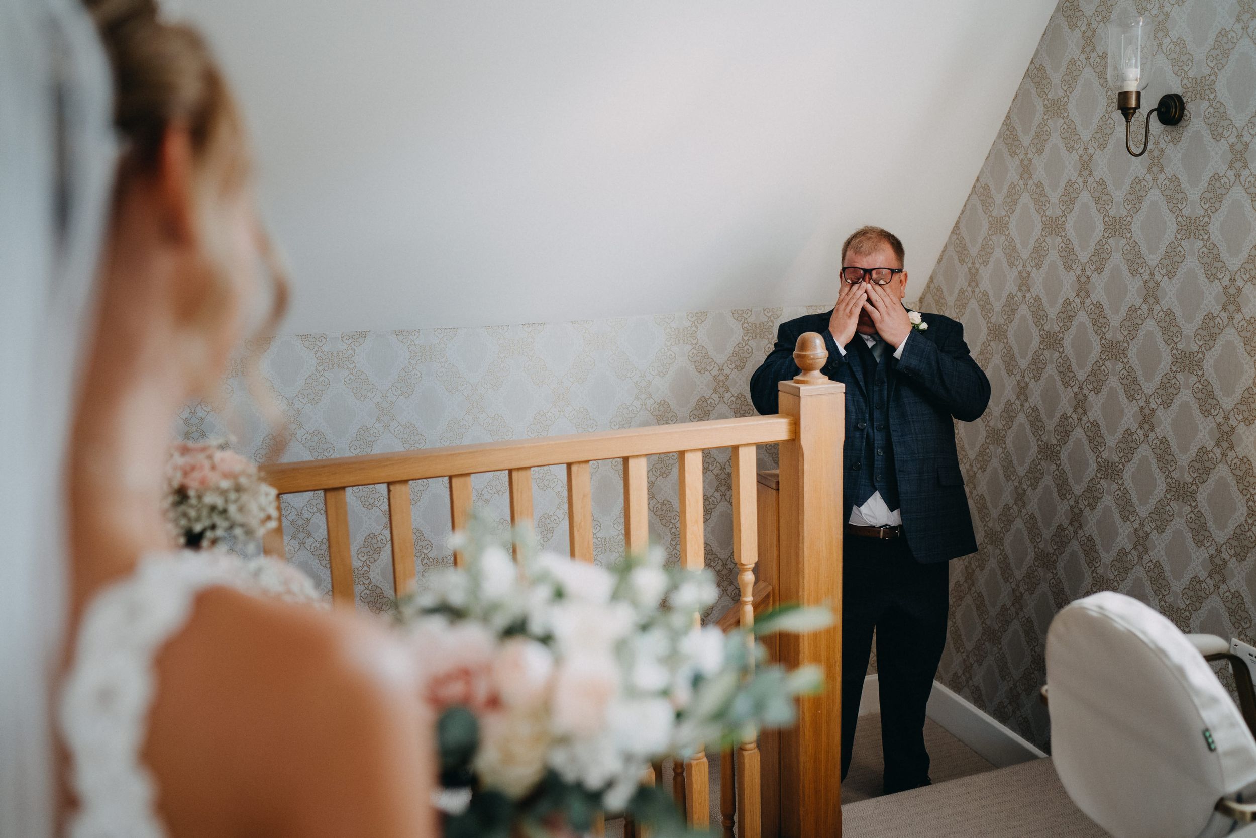 Emotional first look moment captured on wooden staircase during wedding preparations.