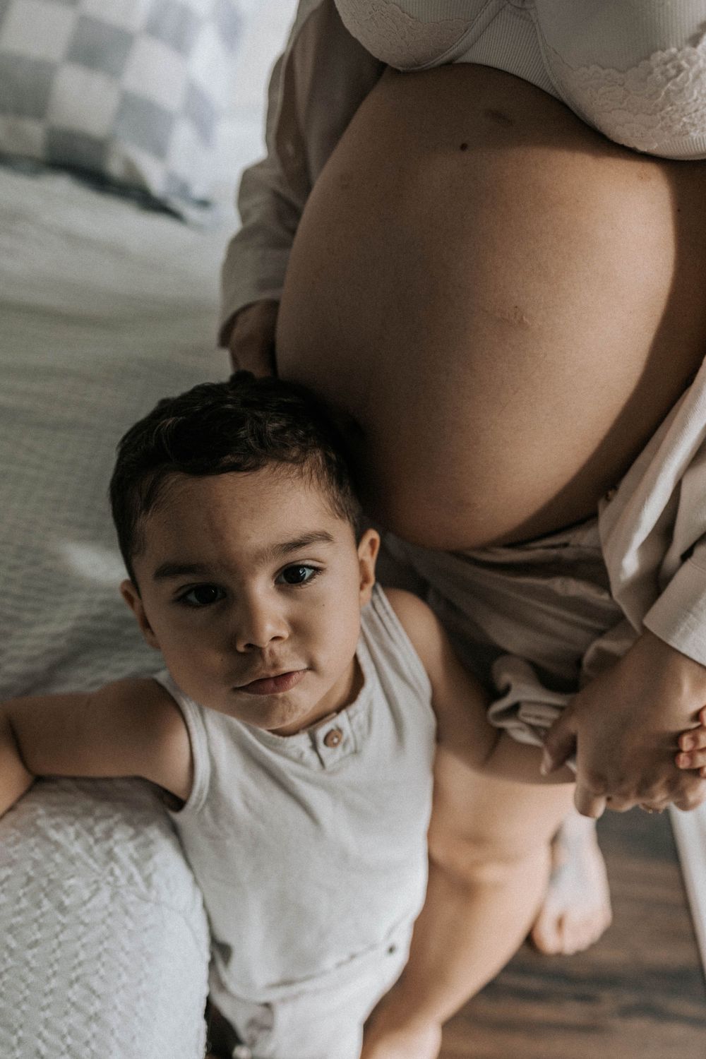 older son looking up while holding his pregnant mother's hand in her bedroom in York, Toronto
