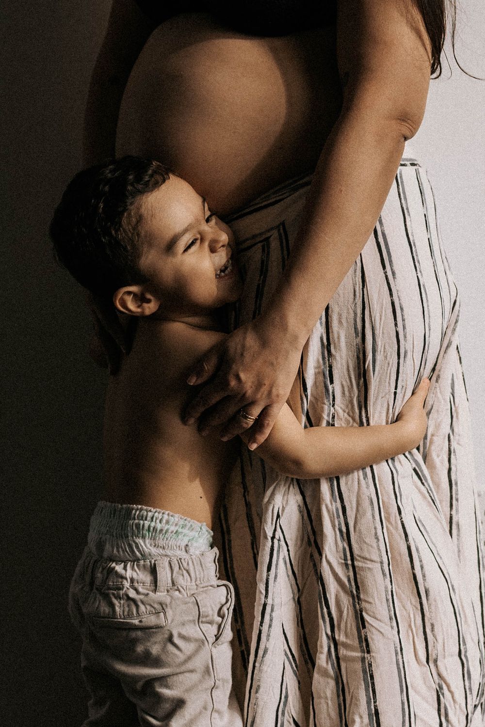 older son hugging pregnant mother's legs for a family photoshoot in their living room in York, Toronto