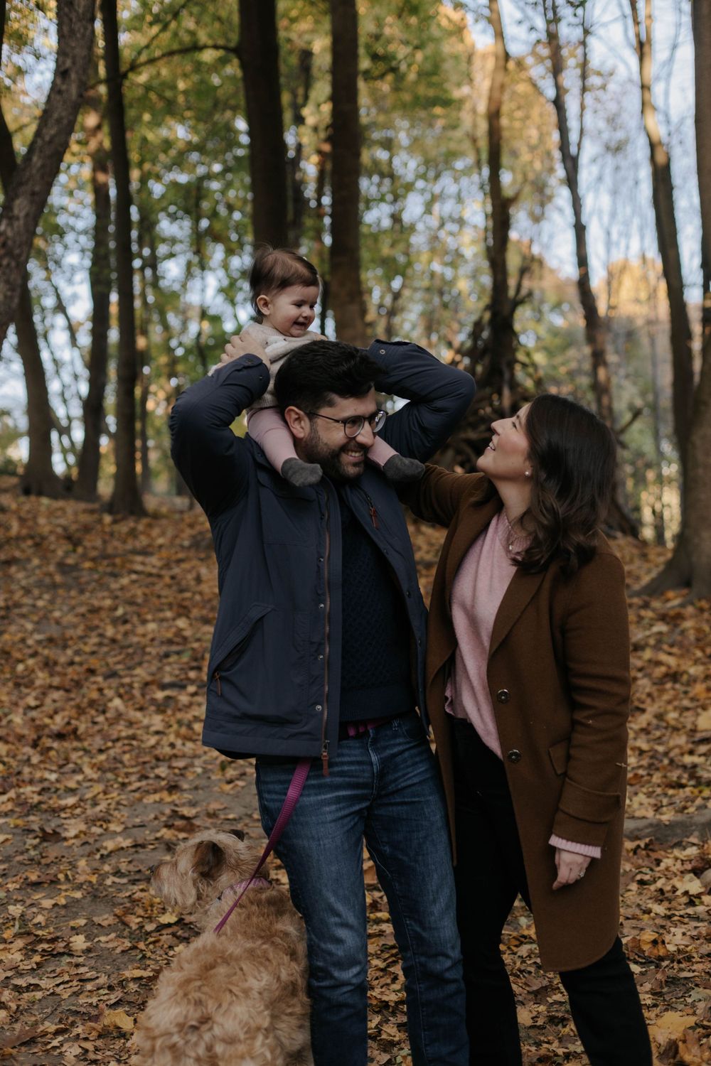 Dad putting his 7 month baby in his shoulder while mother looks at the baby and smile, at park in Toronto.