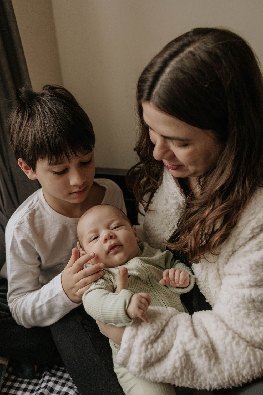 mother and ther 8 years old son looking to her newborn baby in their living room, in Etobicoke, Toronto