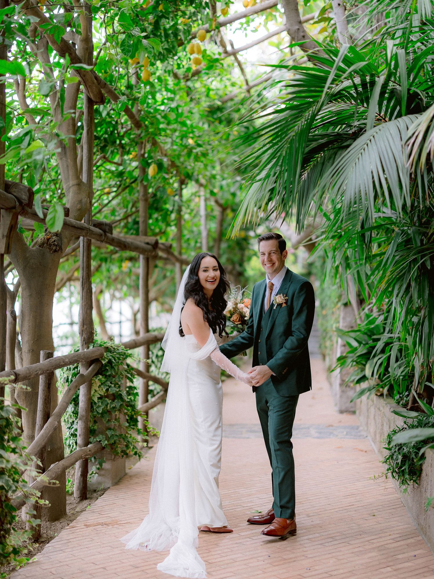 Wedding couple holding hands on a garden path surrounded by lush tropical plants and greenery at Hotel Santa Caterina.
