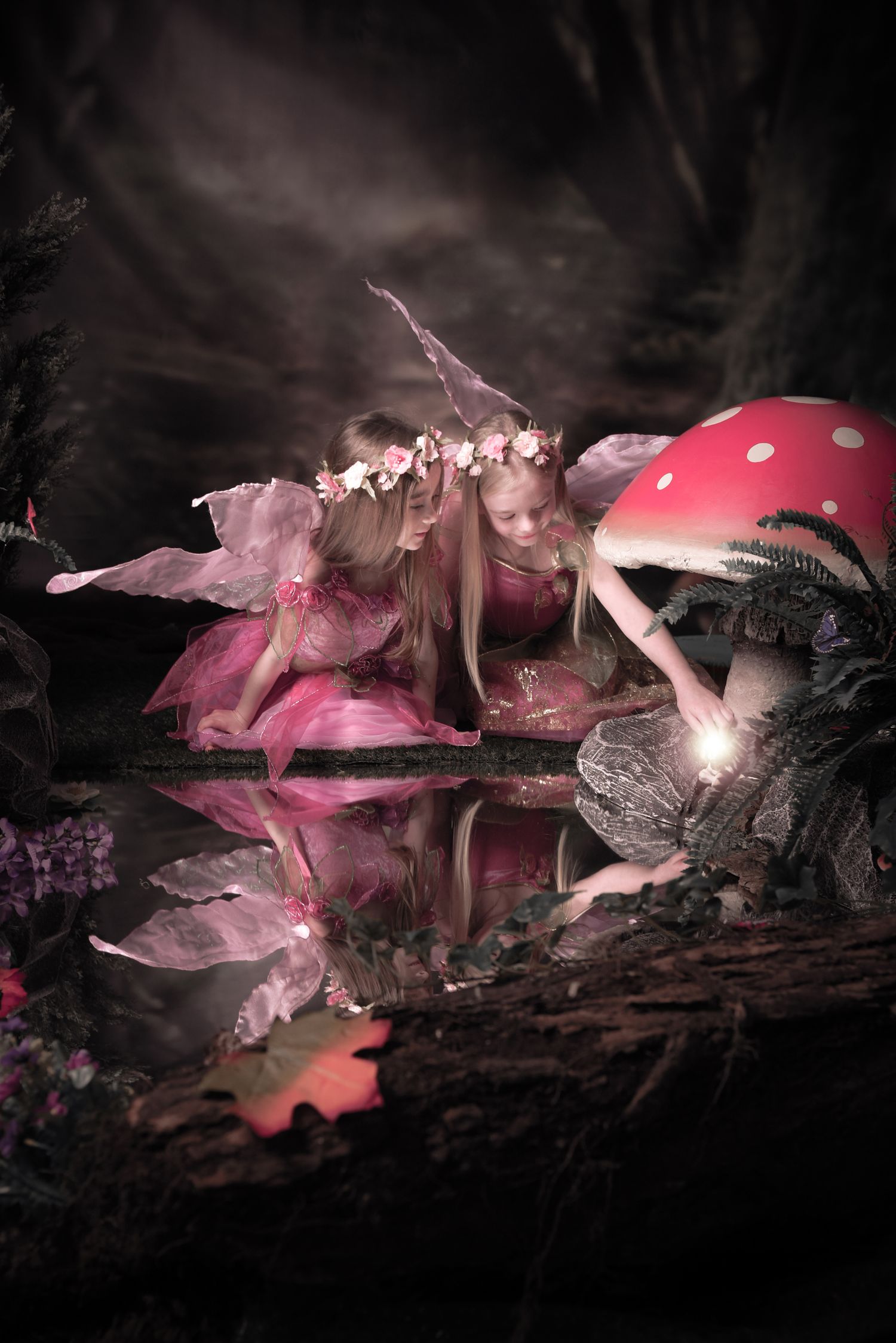 Ethereal fairy scene with pink dresses and red mushrooms reflected in dark woodland waters.