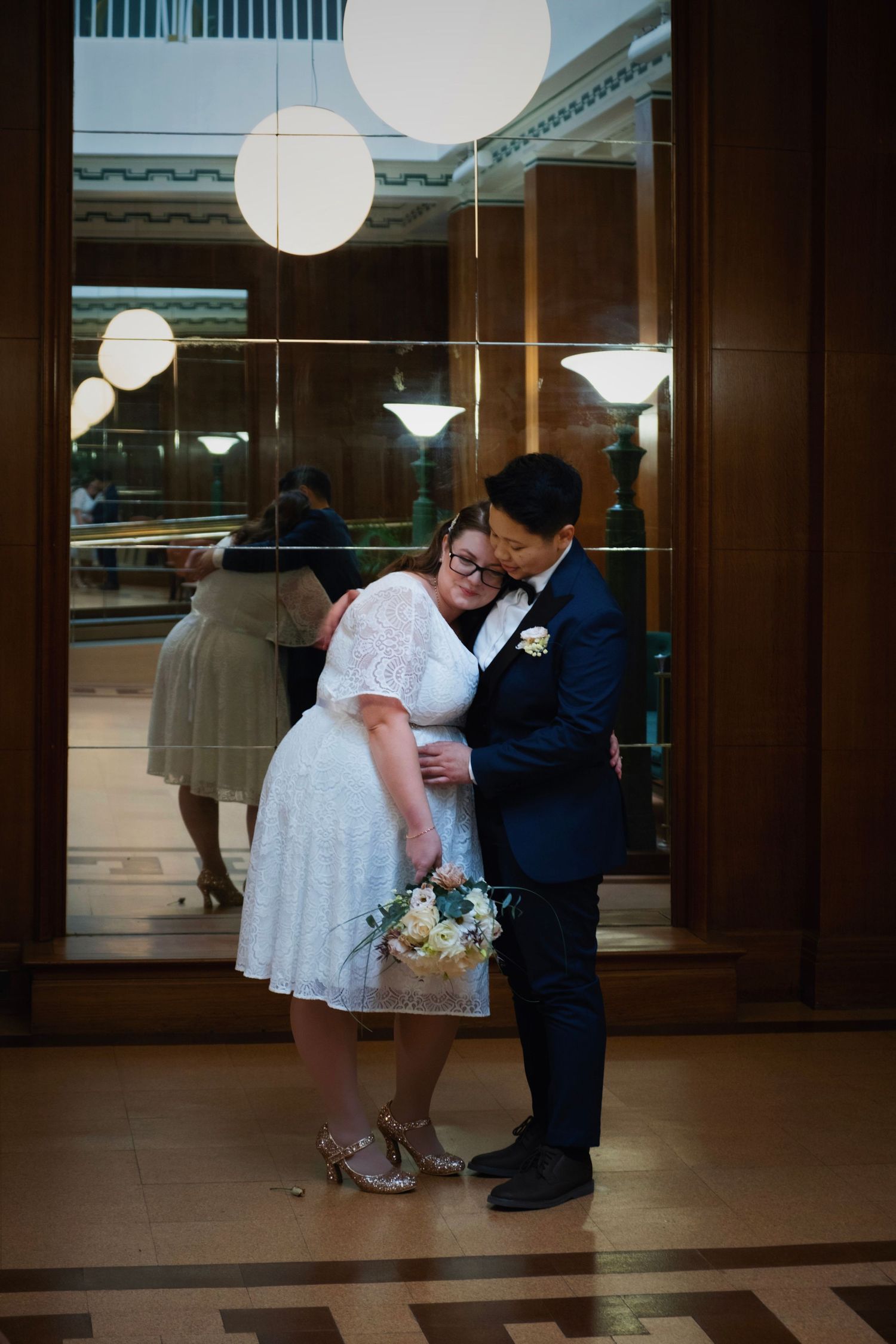 Couple sharing intimate moment in formal wear under elegant pendant lighting.