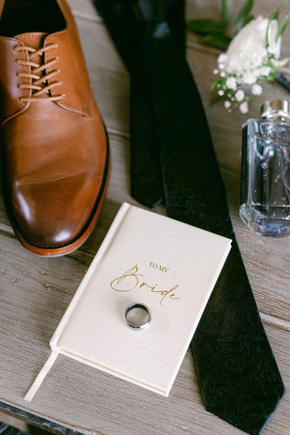 Wedding details featuring brown leather shoes, black tie, and elegant stationery with gold lettering.