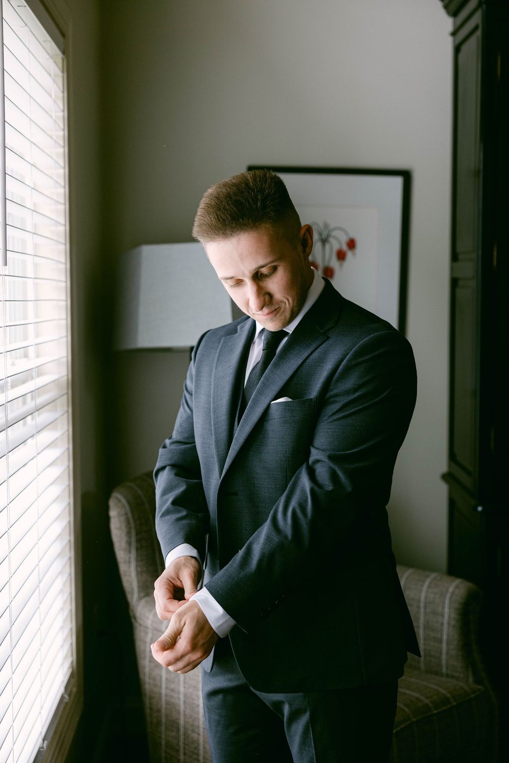 Wedding preparation scene showing someone adjusting formal attire by a window.