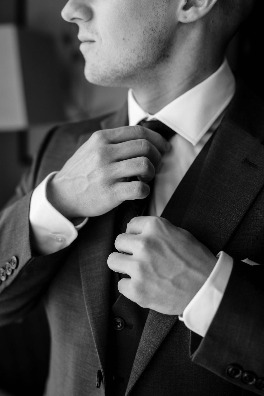Close-up black and white photo of hands adjusting a tie and suit jacket.
