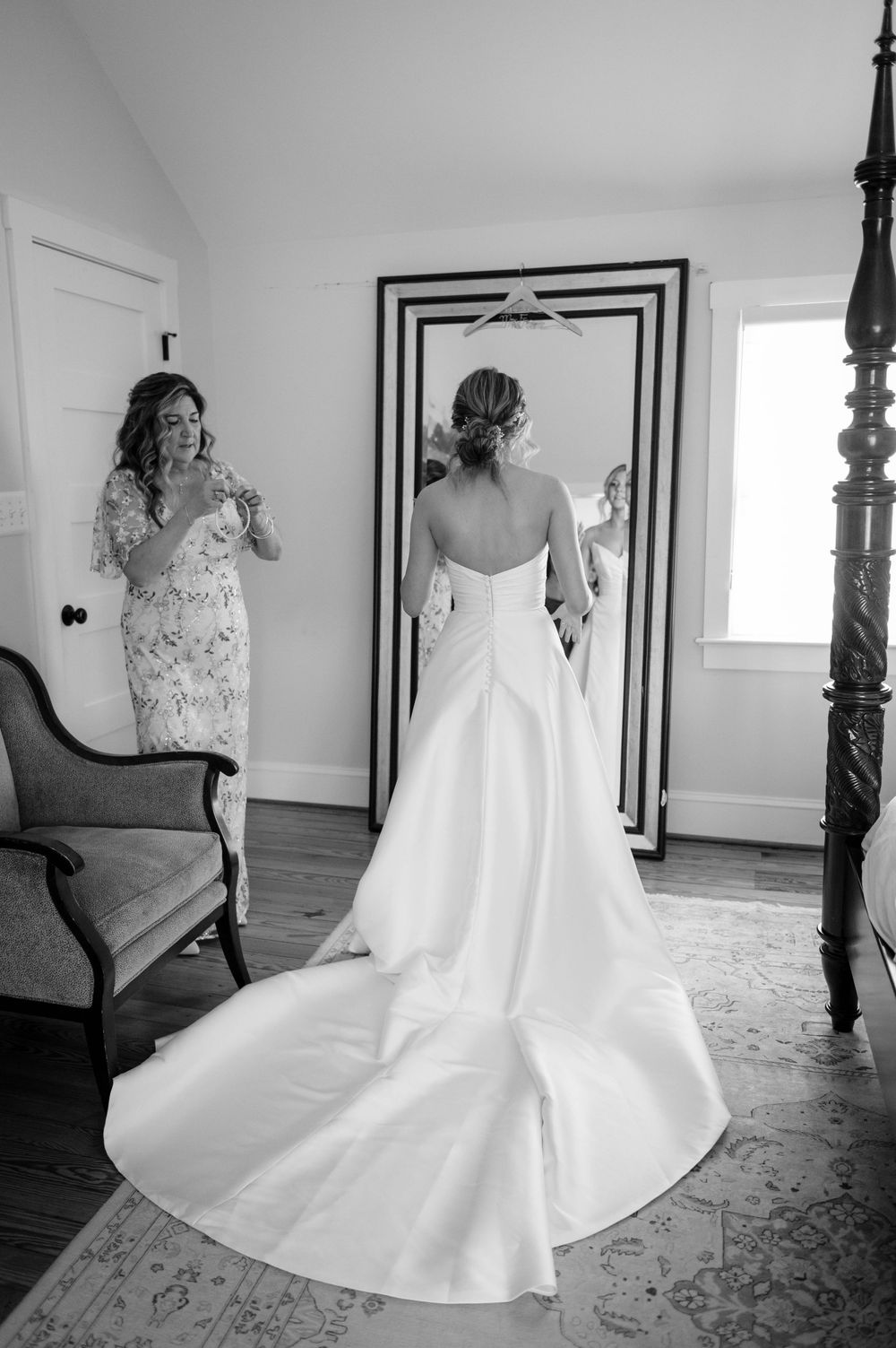 Black and white photo of elegant wedding dress with long train in front of framed mirror.