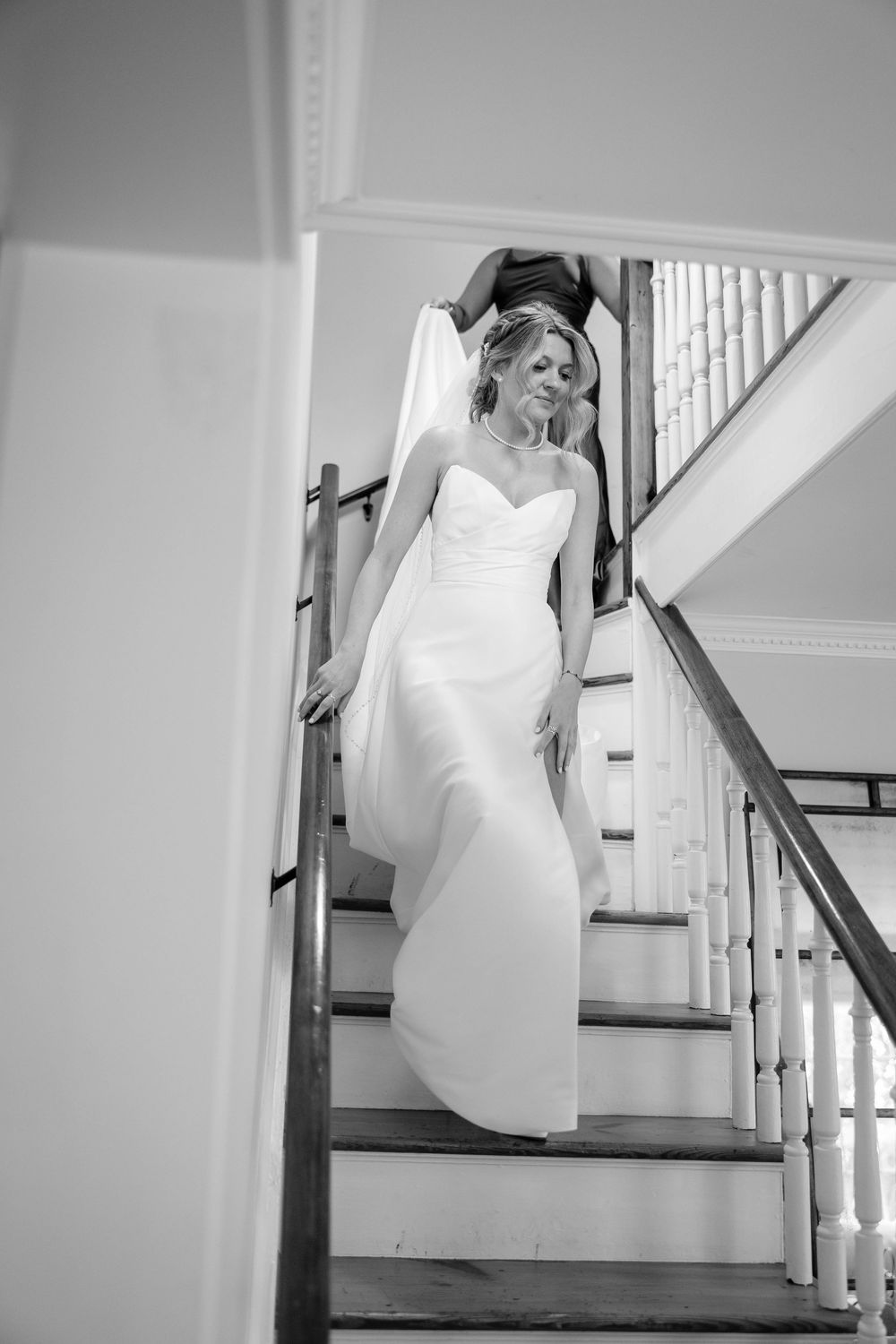 Black and white photo of bride in fitted wedding dress descending staircase.