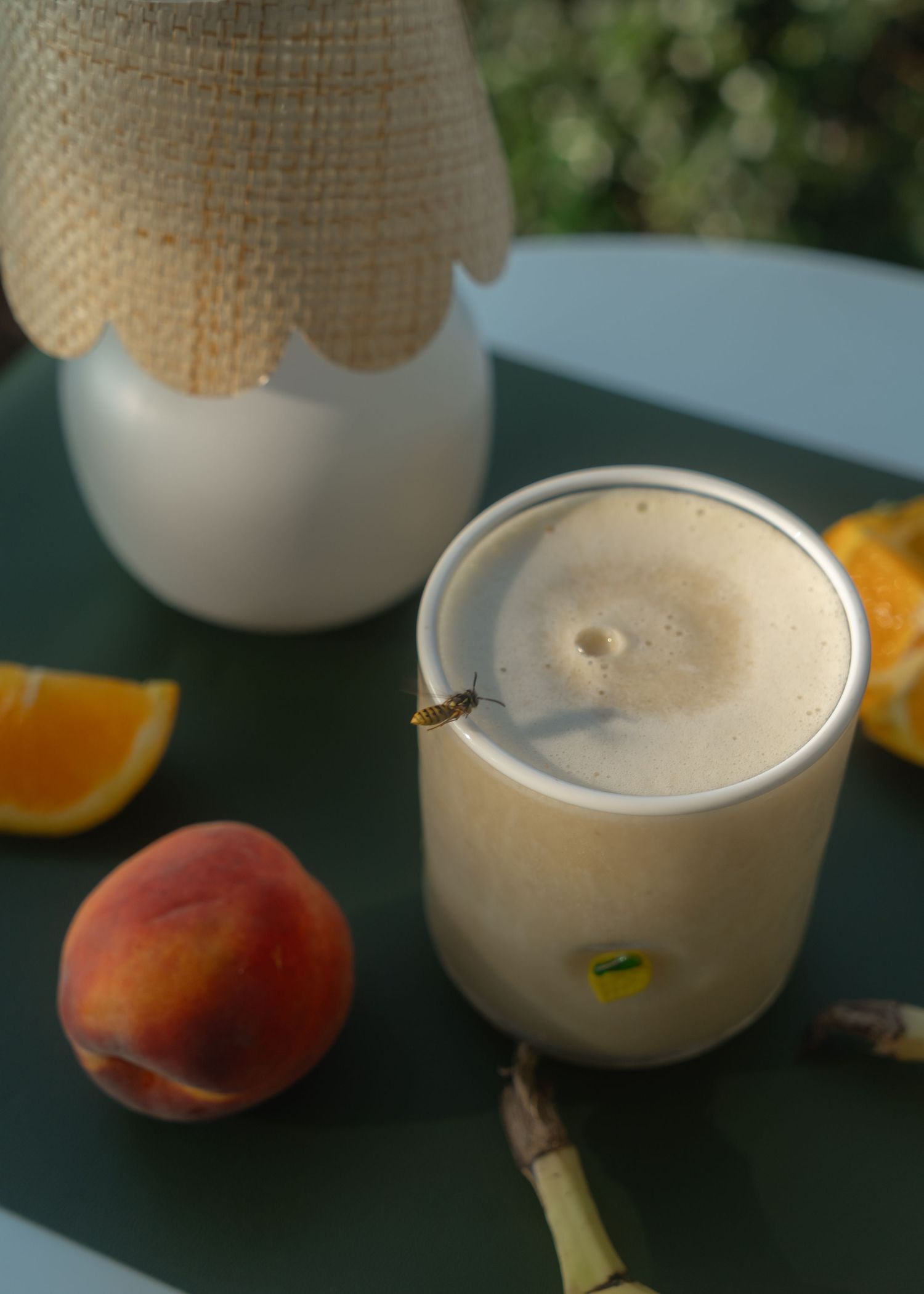 summer smoothie in clear glass cup with bee buzzing on rim