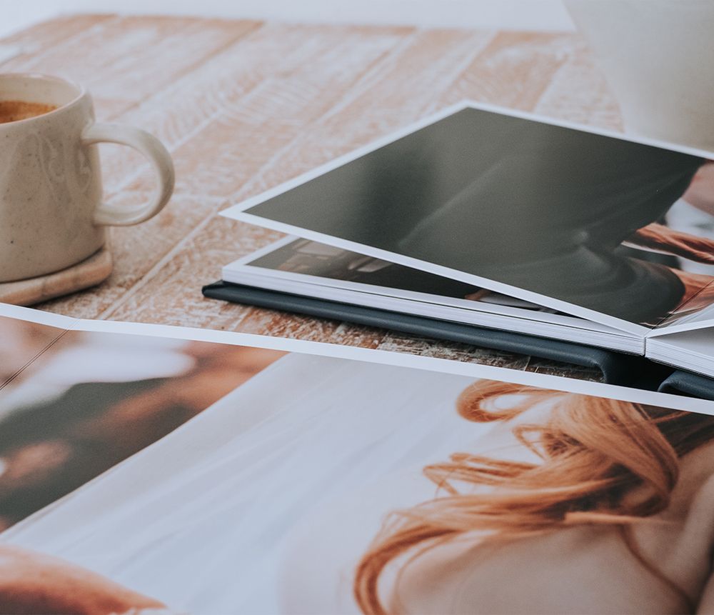 Coffee cup and photographs scattered on a wooden surface with soft natural lighting creating a cozy atmosphere.