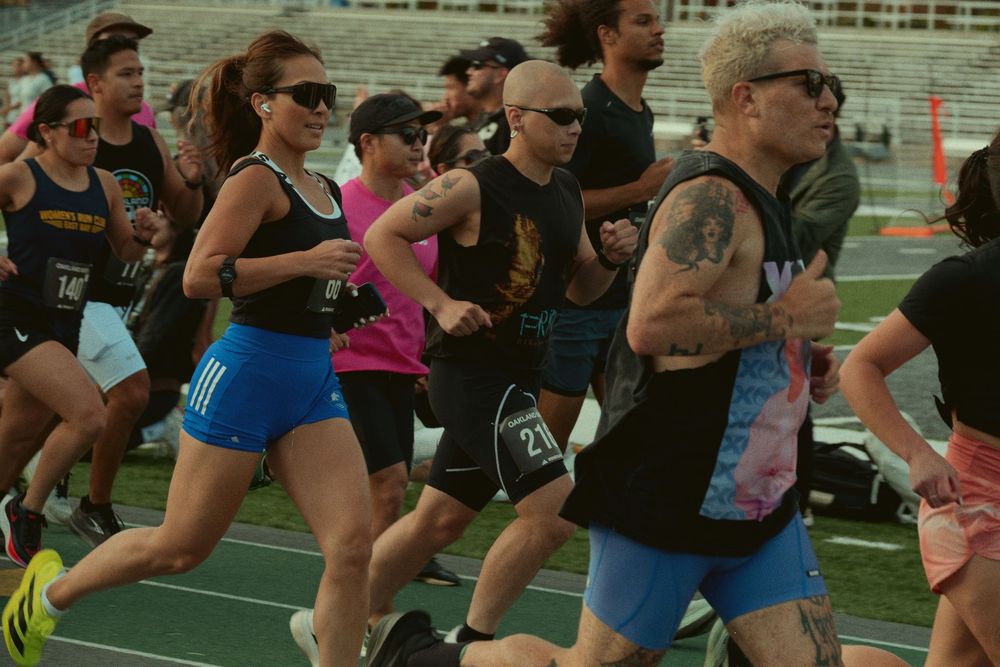 A group of runners compete in an outdoor race on a track during a sunny day.
