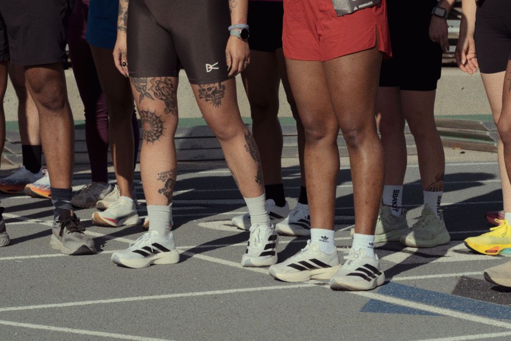 Group of people wearing different athletic shorts and sneakers standing on pavement in sunlight.