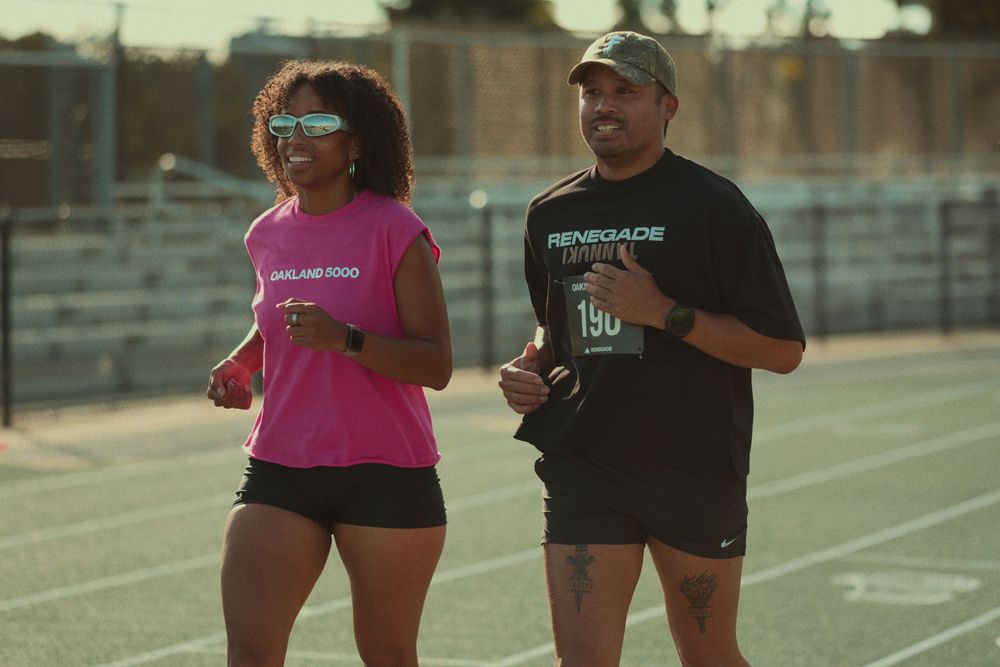 Two runners in athletic gear train together on an outdoor track in warm evening light.