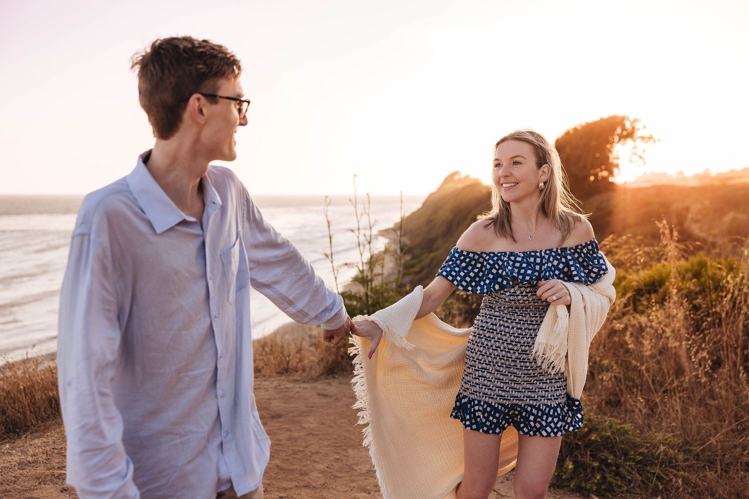 A romantic couple just finished a surprise proposal on Ellwood Bluffa with Ellwood Beach in background at sunset with golden light.