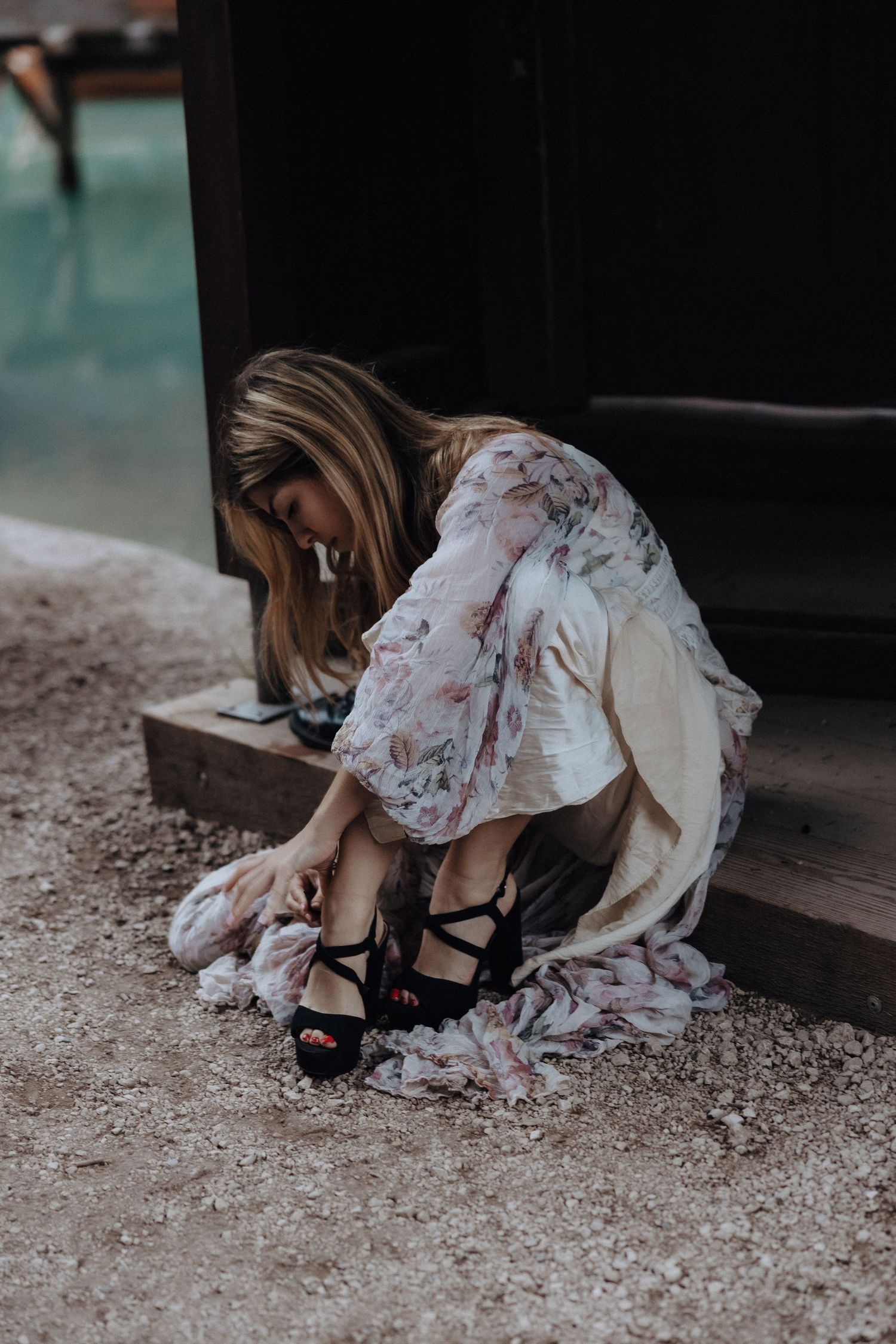 A woman in a floral dress and black heels sits on rough ground in a moody photographic series.