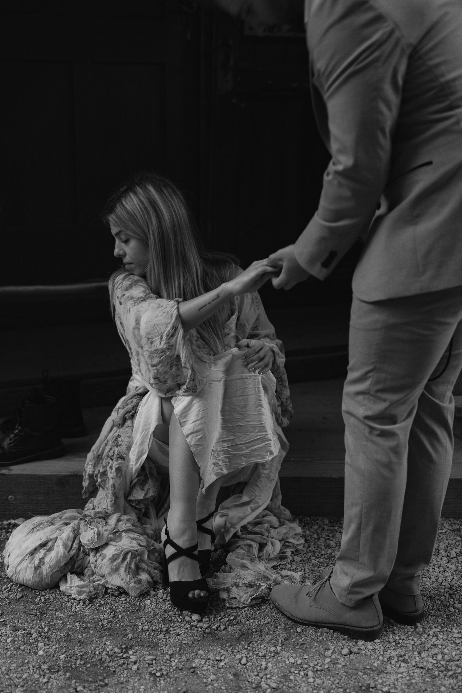 A black and white artistic photo showing someone in a flowing dress being helped up by another person.