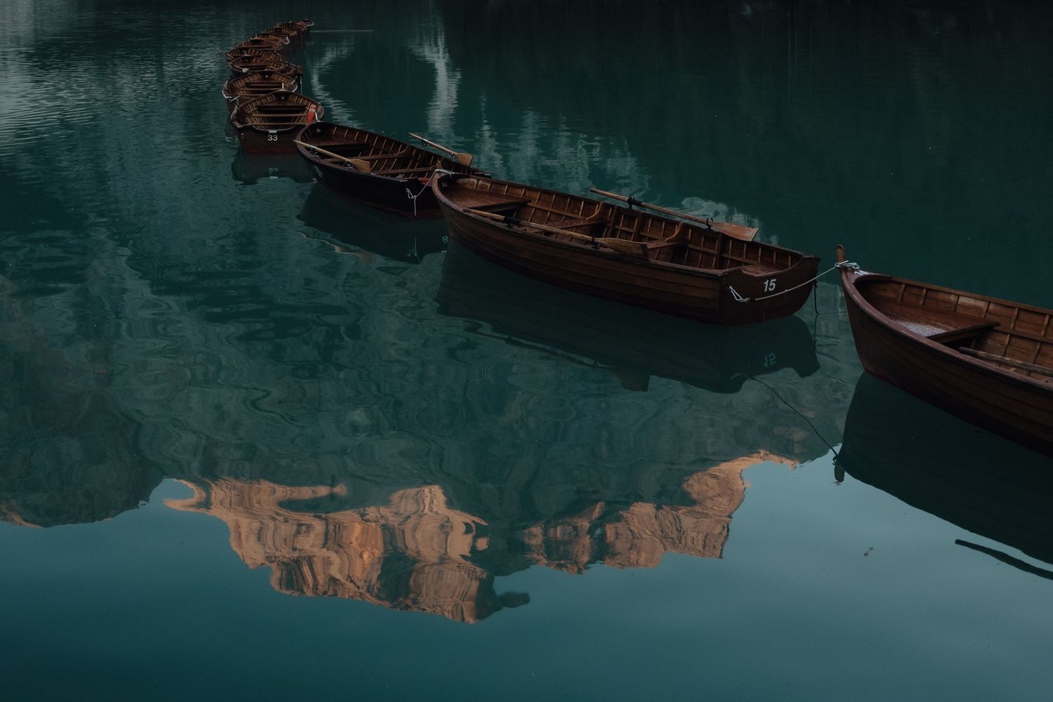 Wooden boats float on calm turquoise water with orange cliffs reflecting in the mirrored surface at sunrise.