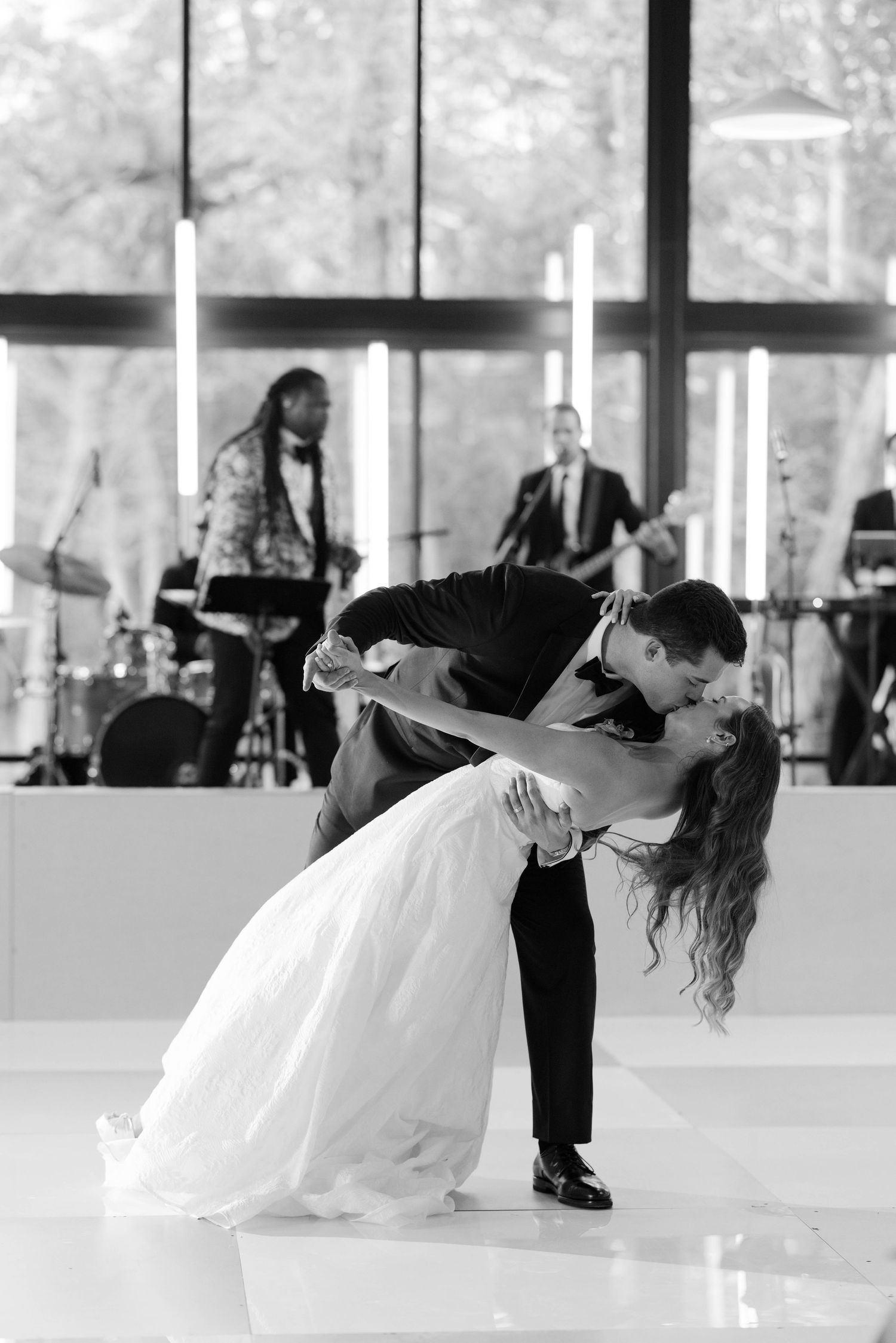 A couple performs a romantic dip during their first dance at a wedding reception with a live band in the background.