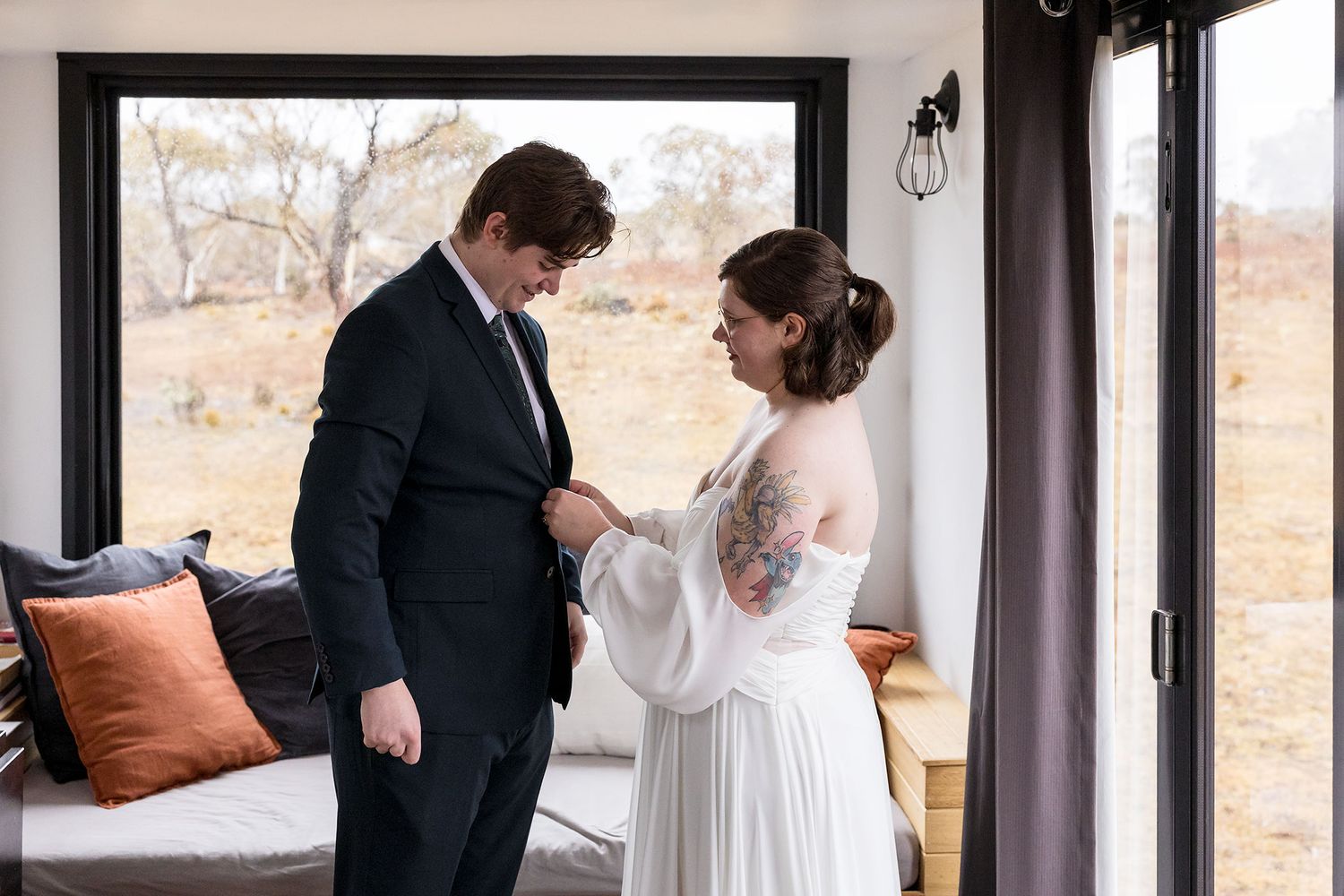 A couple shares an intimate first look moment in their wedding attire by a large window.