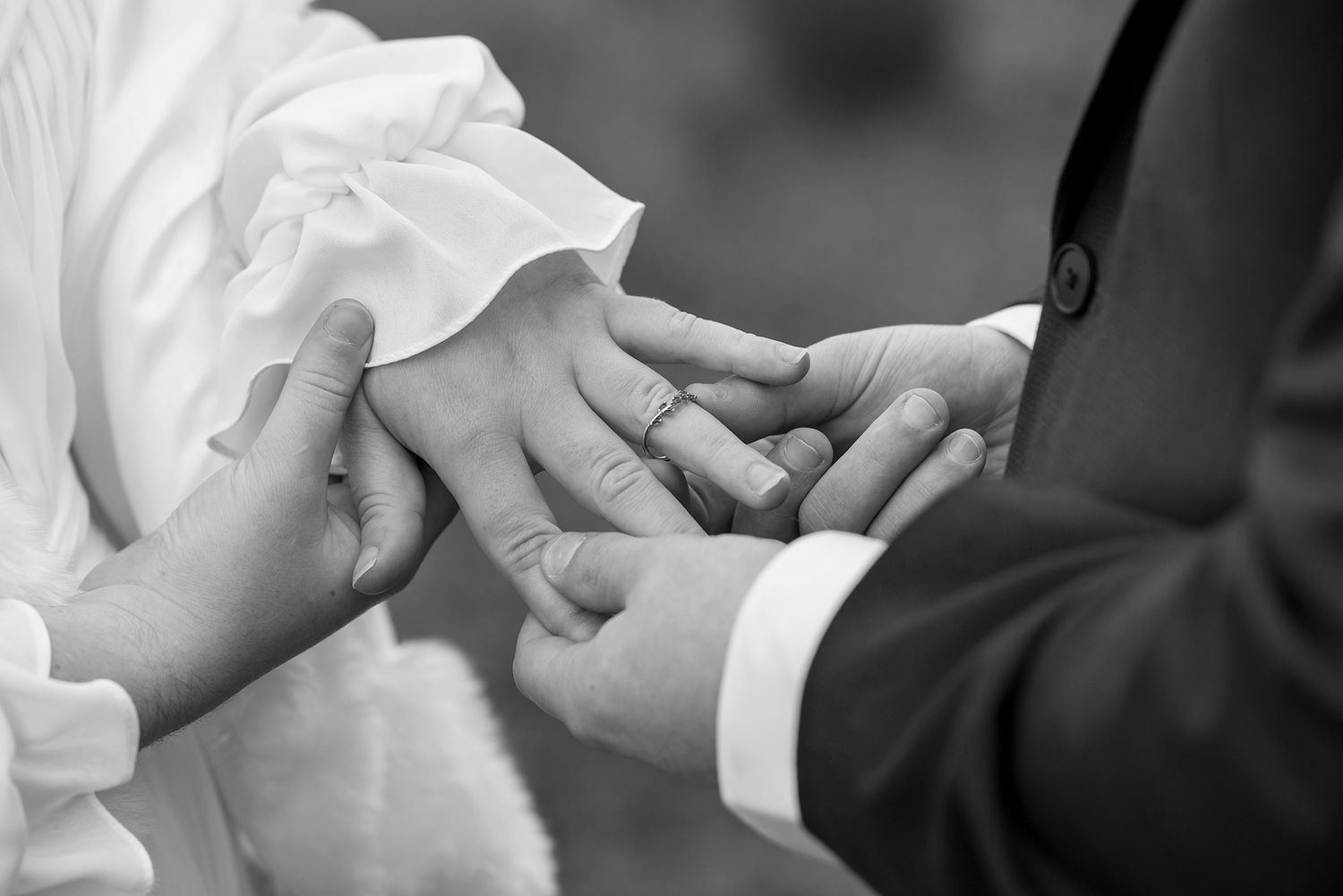 Black and white close-up of hands exchanging wedding rings during a marriage ceremony.