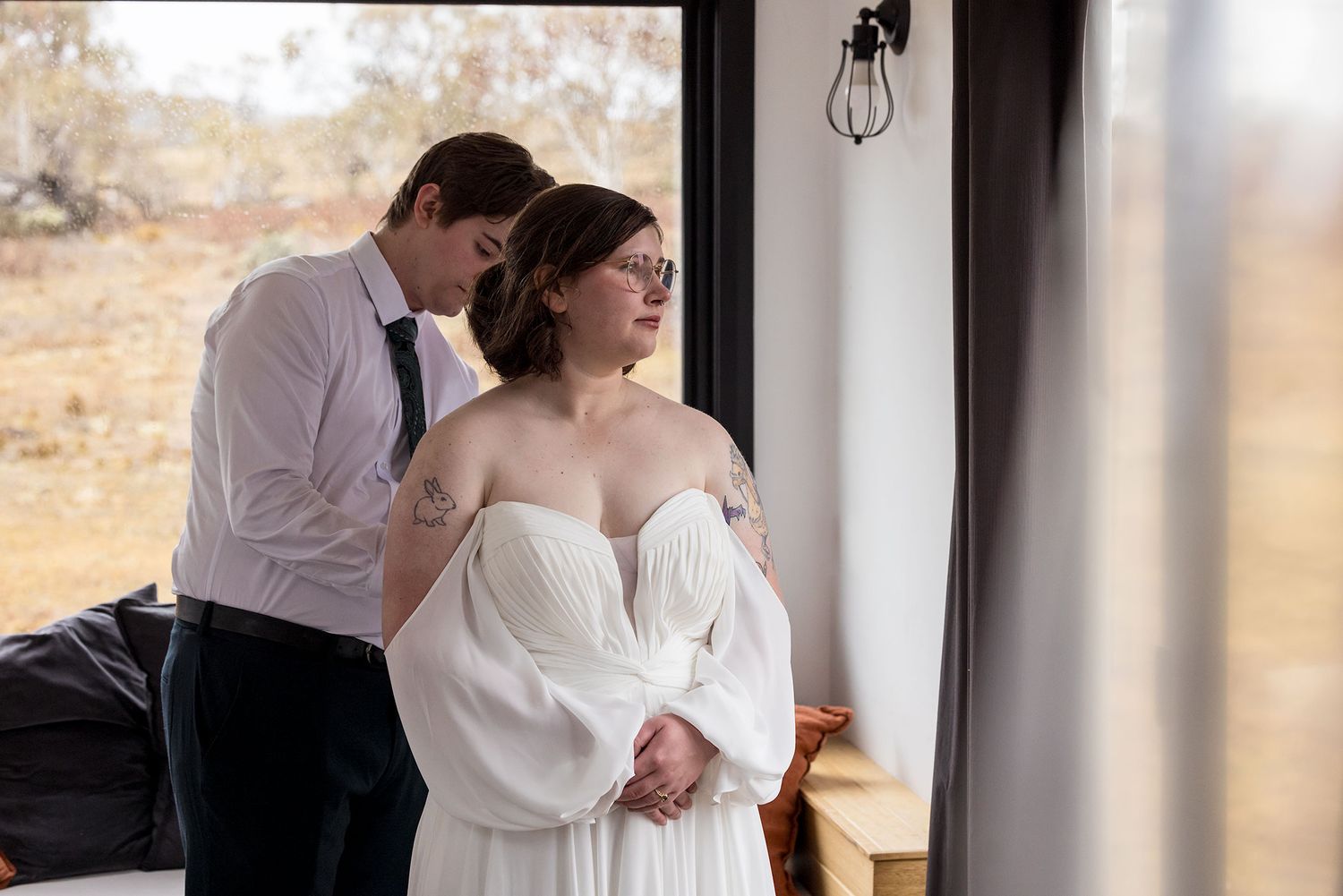A couple shares an intimate moment in their wedding attire beside a window with natural lighting before their Jindabyne Snow Elopement.