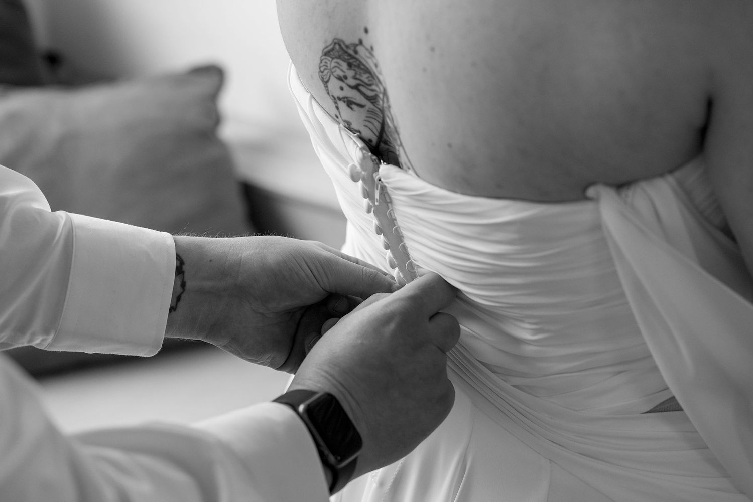 A close up image of a Groom helping his Bride with her Dress buttons in Black and White.