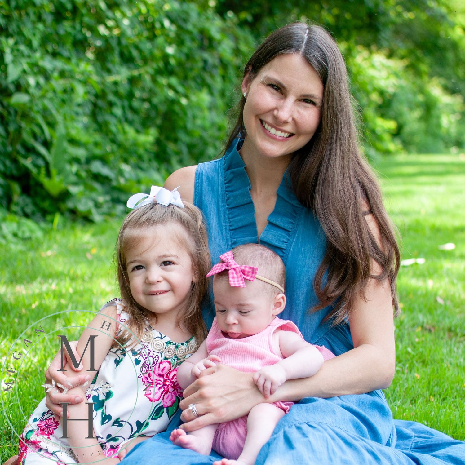 Photo of a mother with a toddler and infant sitting together on green grass at Baron Cameron Park.