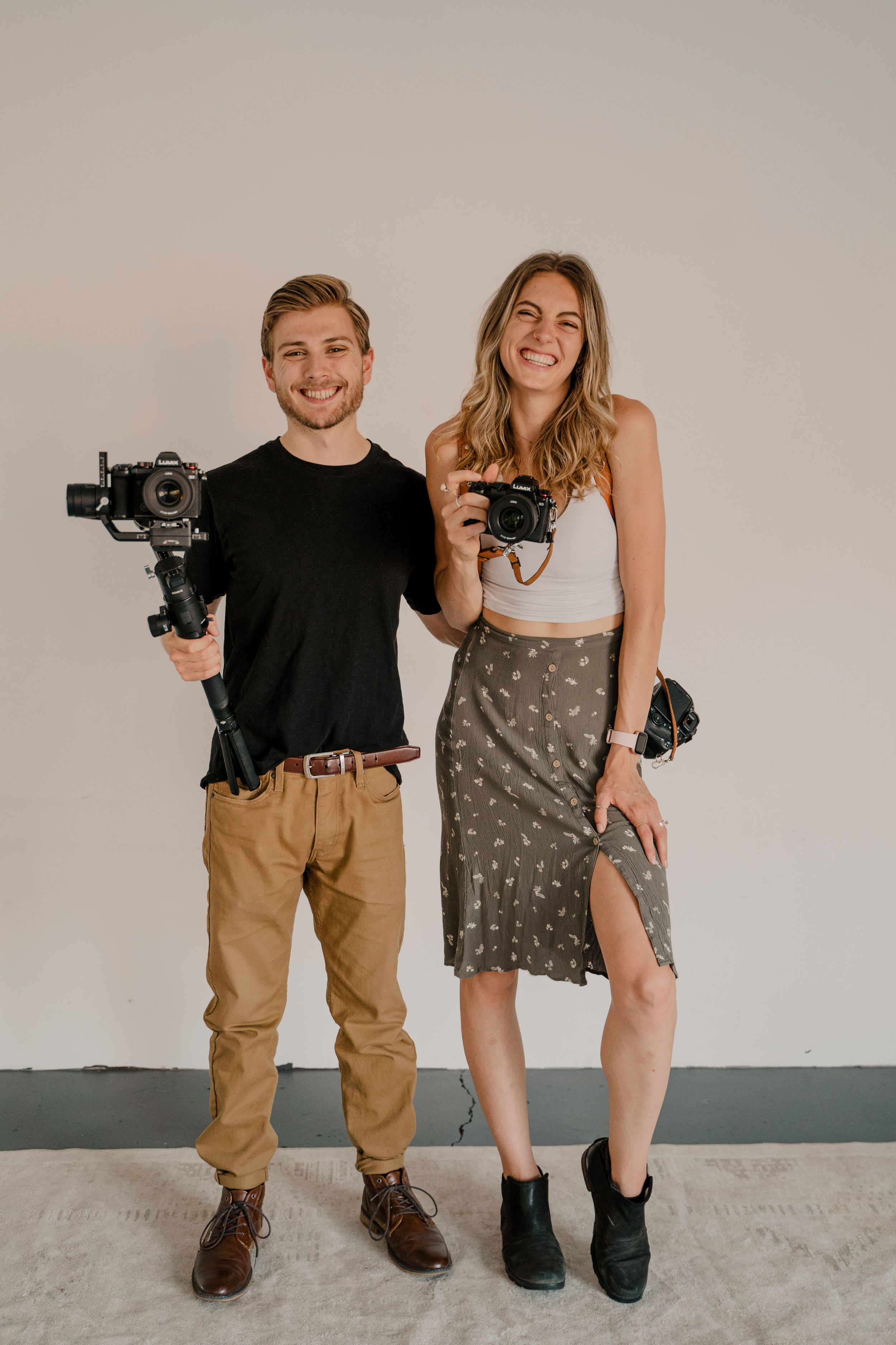 Two photographers smile while displaying their professional camera equipment.