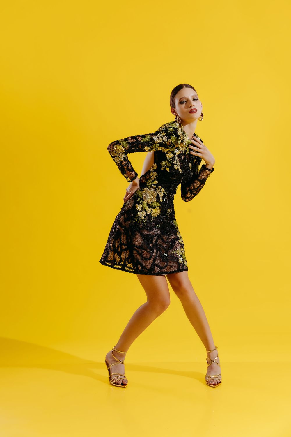 Woman in black lace dress poses dynamically against vibrant yellow background in studio photo series.