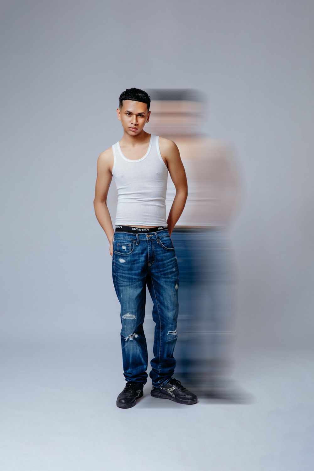Studio fashion photo of a model in white tank top and jeans against grey background.