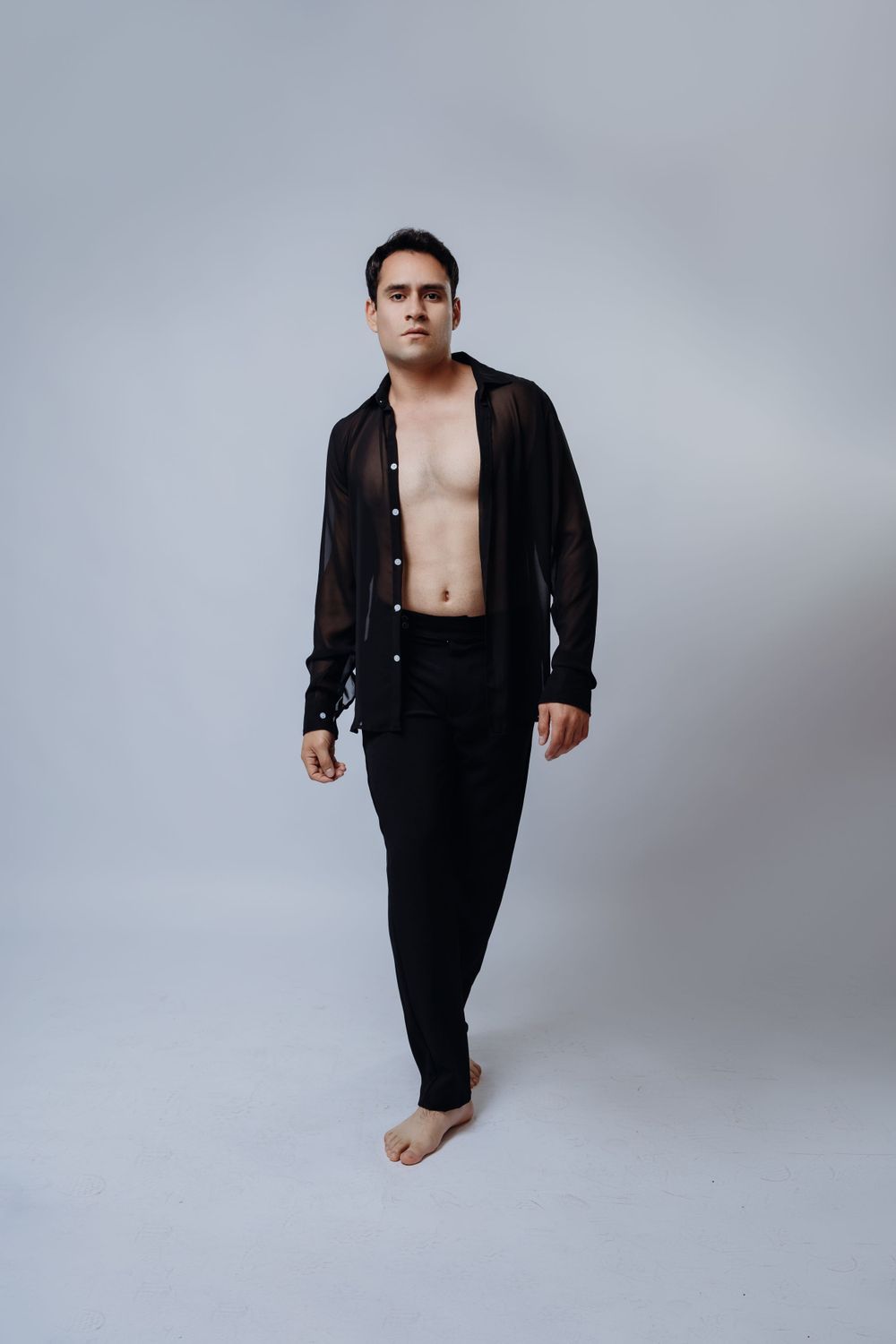 Minimalist fashion pose in black ensemble against grey studio backdrop.