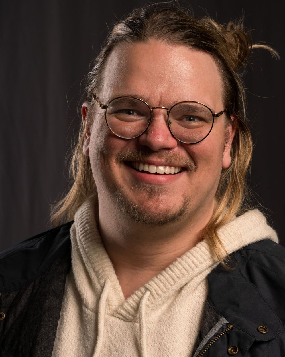 Casual portrait of person in glasses and hoodie with long blonde hair smiling warmly.