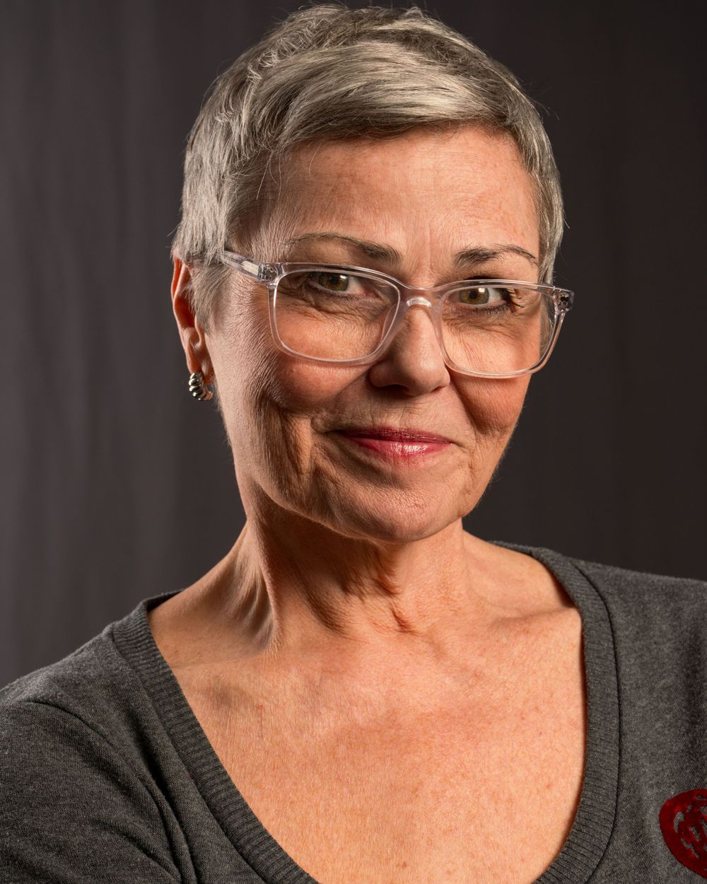 Portrait of person with short gray hair wearing glasses and dark top with red accent.