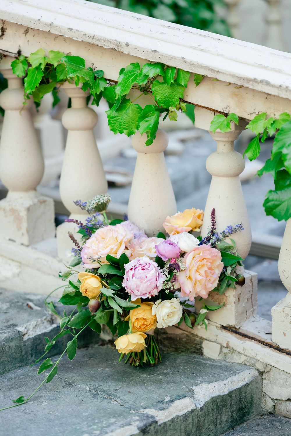 Beautiful floral bouquet with pink and peach roses rests on stone balustrade with ivy.