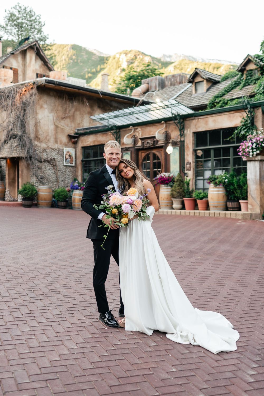 A couple dancing on a brick courtyard in front of a rustic stone building during a wedding celebration.
