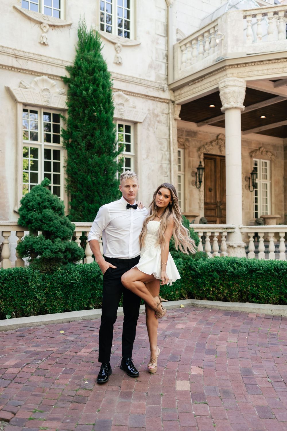 Wedding couple recreates iconic dance move outside elegant stone courtyard with pillars and cypress trees.