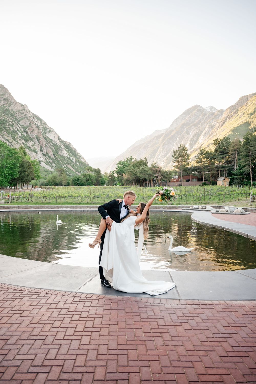 Romantic mountain lake scene with couple dancing on brick patio surrounded by dramatic peaks.