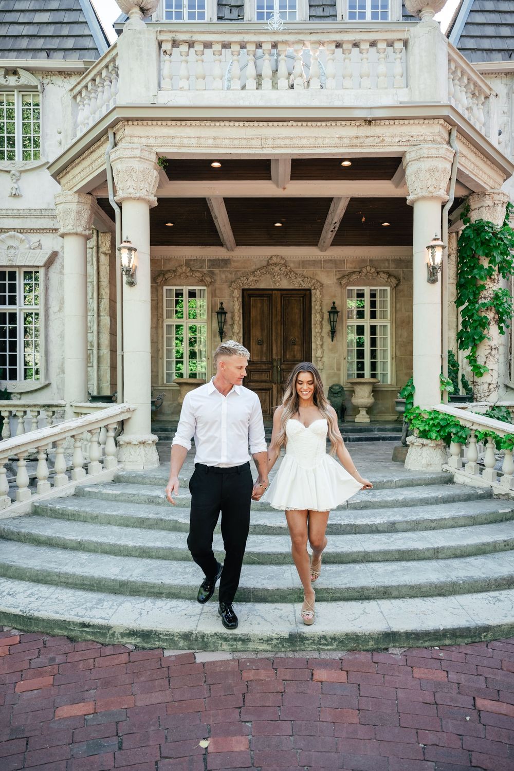 Couple walking together on stone steps of an elegant mansion with classical architecture.