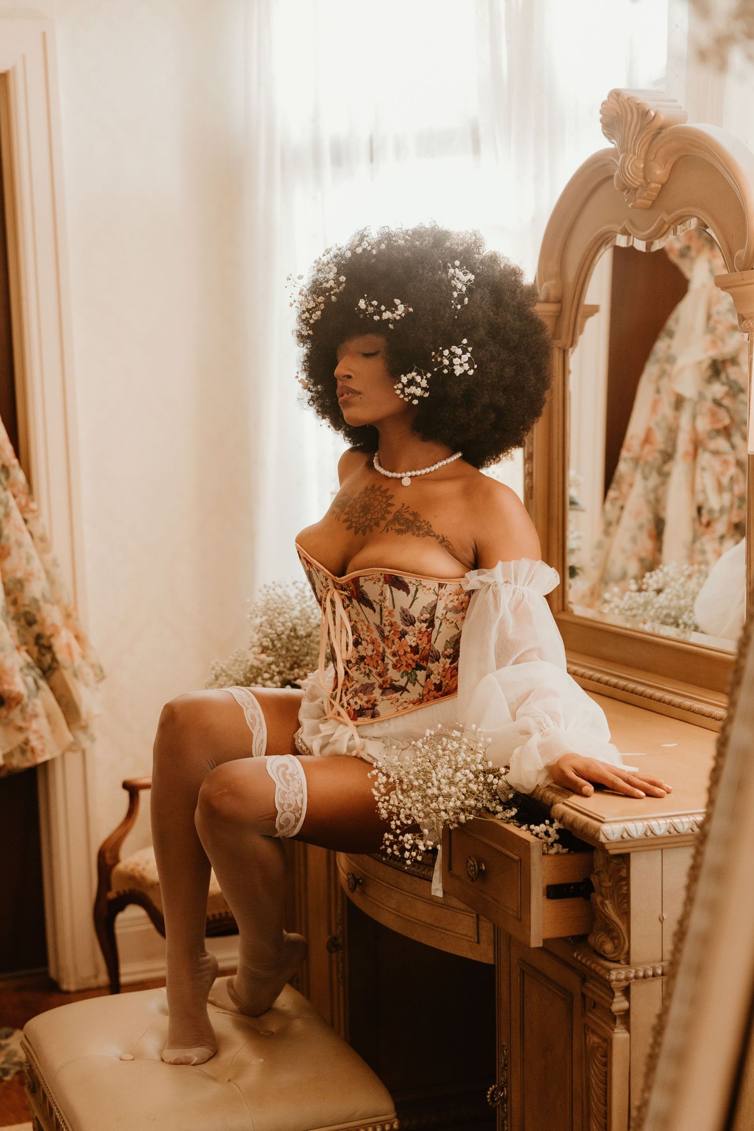 A vintage boudoir photoshoot featuring a corset, lace stockings, and delicate white flowers in a dreamy sepia-toned setting.